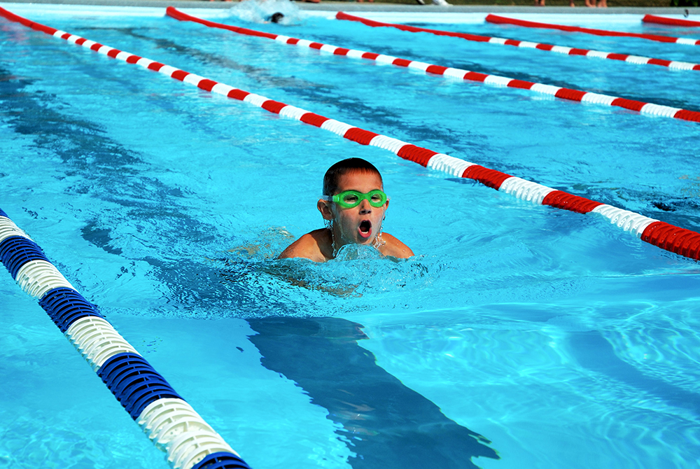Junge mit grüner Schwimmbrille schwimmt in einem Schwimmbecken.